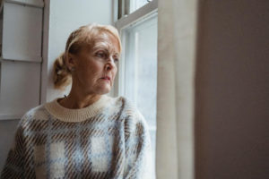 Elderly woman looking out of a window sadly